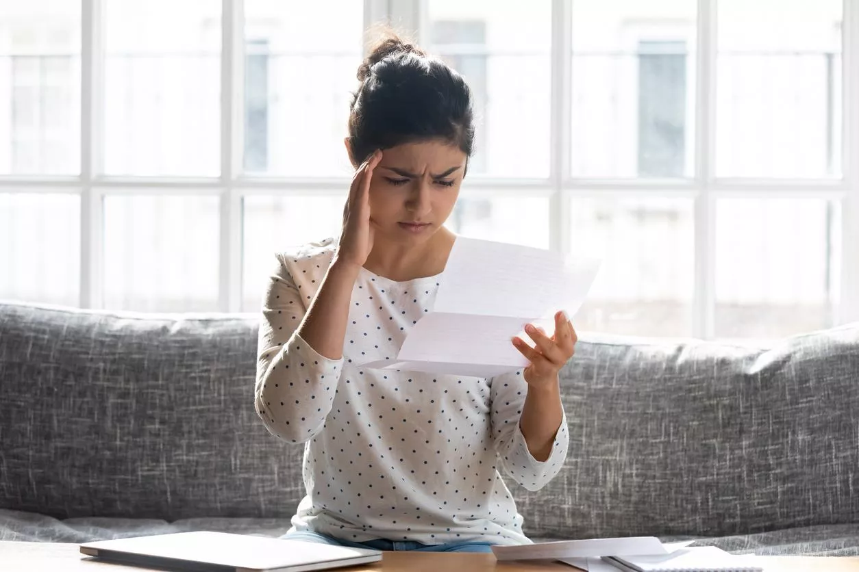 A woman is sitting on a couch and holding a paper bills